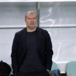 Sean Sogliano in primo piano, con le mani in tasca e in piedi davanti a una panchina